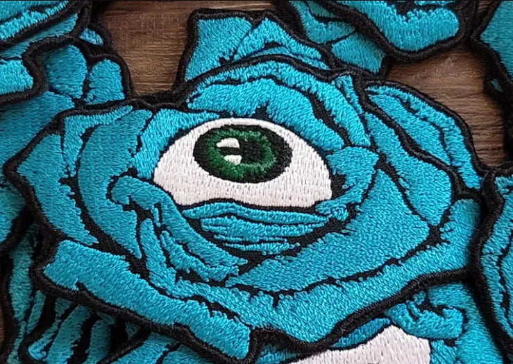 Embroidered patch of blue rose with eyeball in center