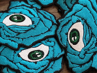 Multiple embroidered patches of blue rose with eyeball in center