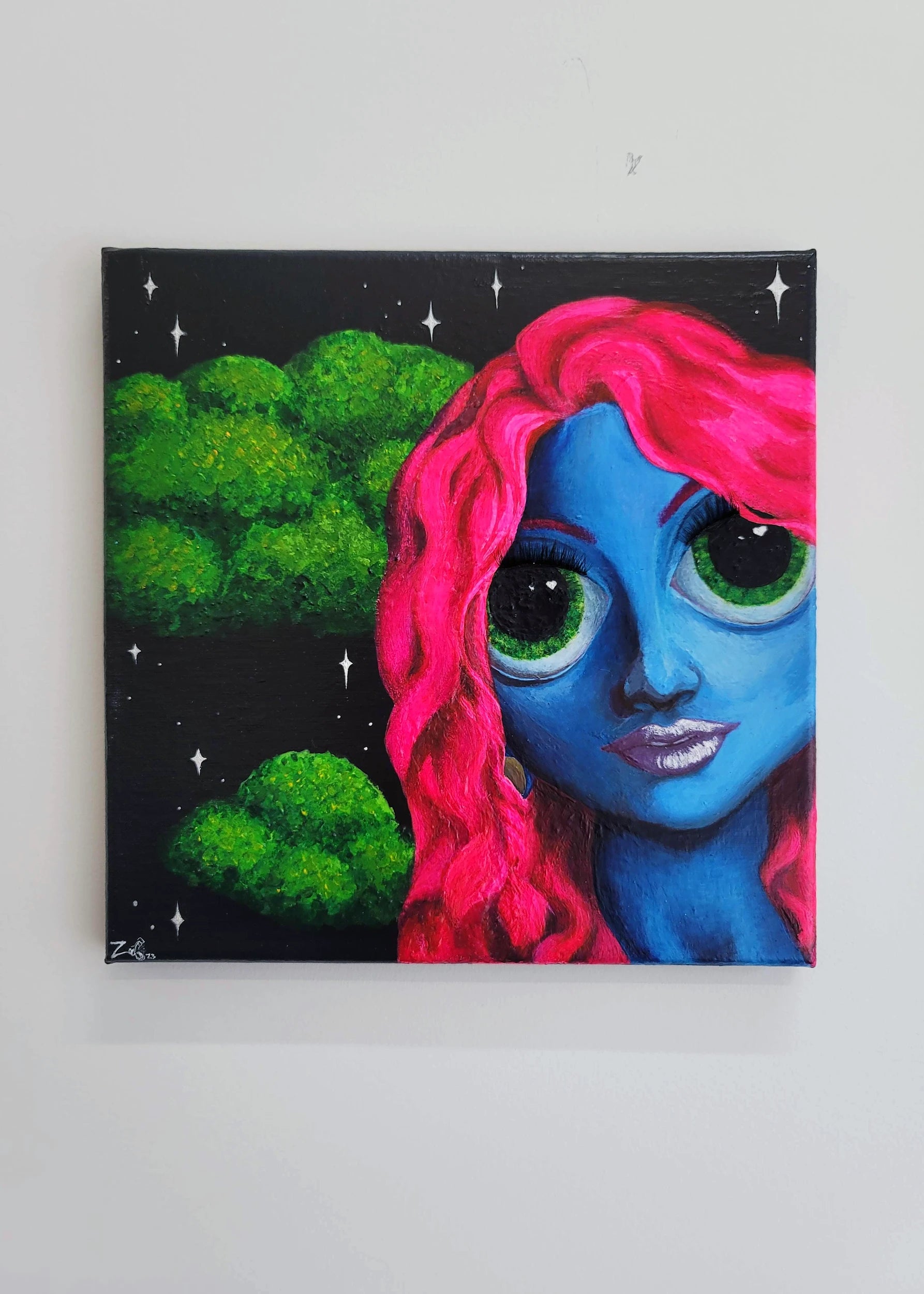 Hanging on the wall is a painting of a girl with blue skin and neon pink wavy hair. She is looking directly back at  the viewer with huge bright green eyes that are similar in color to the tree-like clouds behind her. The background is black and full of stars. She has a very long neck. purple lips, and 3-D eyelashes applied to the canvas. The colors  are all very rich and bold.