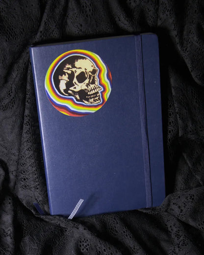 round sticker of skull with a rainbow background, displayed on journal cover.