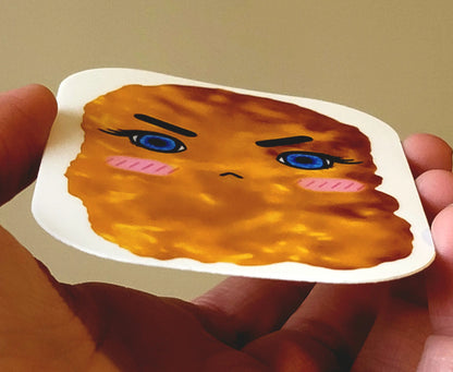 a sticker of the signature logo design: a grumpy chicken nugget. sticker is shown from the bottom, and is being held by a white hand.