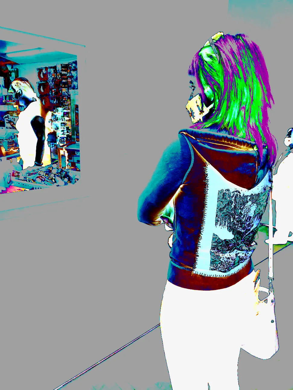 woman is standing, facing away from camera at an angle, with arms folded while looking at art in a museum. she wears a hoodie with a back-patch and a decorative face mask. image edited to invert color scheme and increase contrast, giving it a 'glitchy' feel.